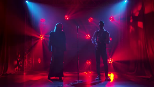 Silhouette a Young Stylish Guy Plays the Saxophone on Stage in the Rays of Red Spotlights. In the alt