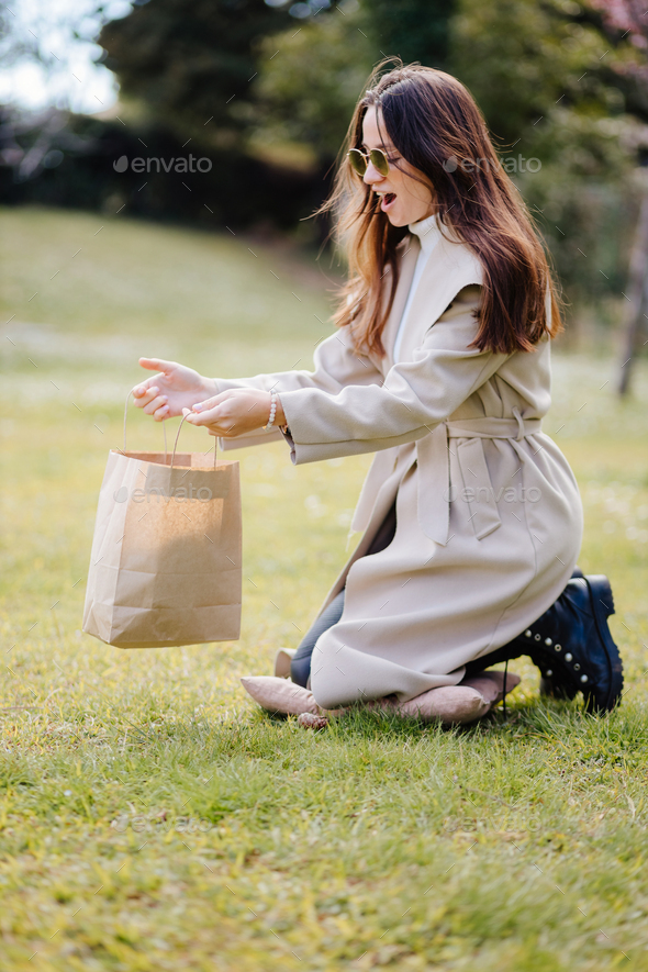 happy young woman holding craft bag present outdoors in park