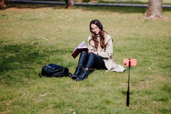 female student virtual learning on mobile outdoors sitting in park