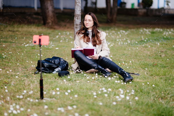 female student virtual learning on mobile outdoors sitting in park