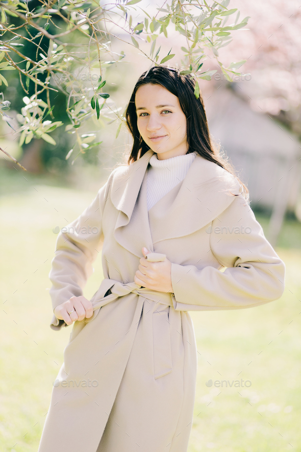 outdoor lifestyle fashion portrait of young woman wearing spring coat - Stock Photo - Images