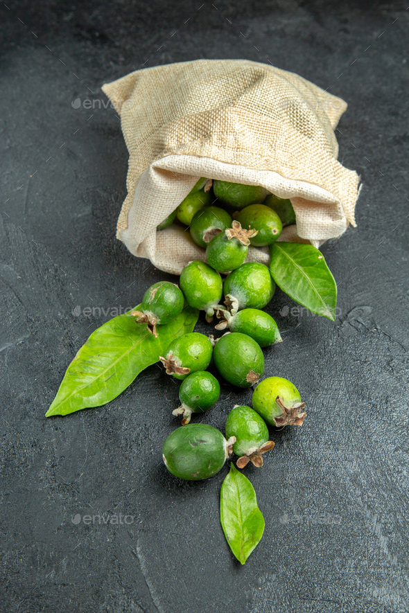 Vertical view of natural fresh green feijoas from a fallen white bag on isolated black background