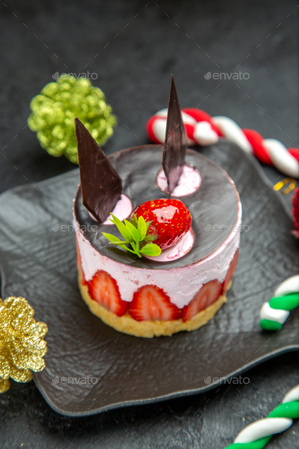 Creamy small cupcake with chocolate and strawberry on a black plate and sweets in the form of