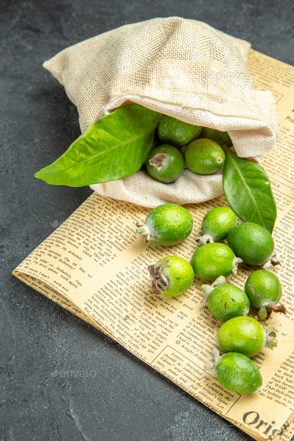 Vertical view of natural fresh green feijoas from a fallen white bag on newspaper on isolated black