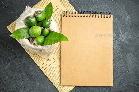Above view of natural fresh green feijoas in a white bag on newspaper and notebook on black table