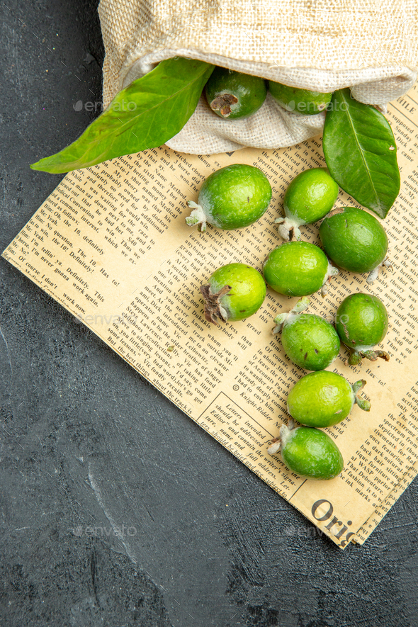 Vertical view of natural fresh green feijoas from a fallen white bag on newspaper on black