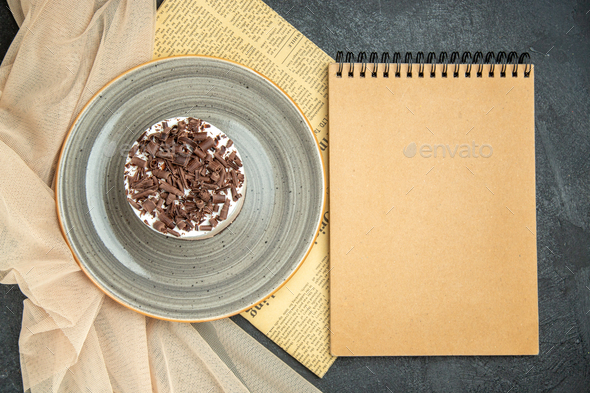 Above view of notebook and creamy homemade small cupcake with chocolate on a small plate on nude