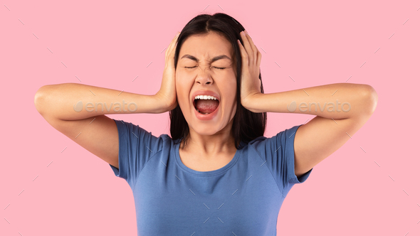 Angry asian woman covering her ears with hands and screaming