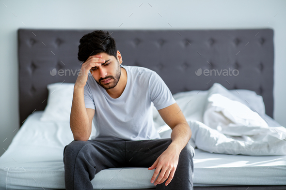 Bad mood in morning. Depressed arab guy sitting on bed and contemplating about problems, copy space