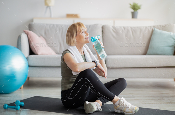 Wellness concept. Fit mature lady drinking fresh clear water from bottle after sports workout at
