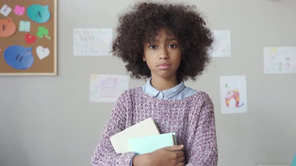 Cute African Kid Girl Looking at Camera Standing in Classroom Holding Books alt