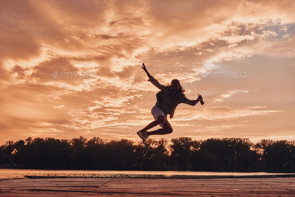 Go wild! Young man hovering against dramatic sky while jumping on the pier - Stock Photo - Images