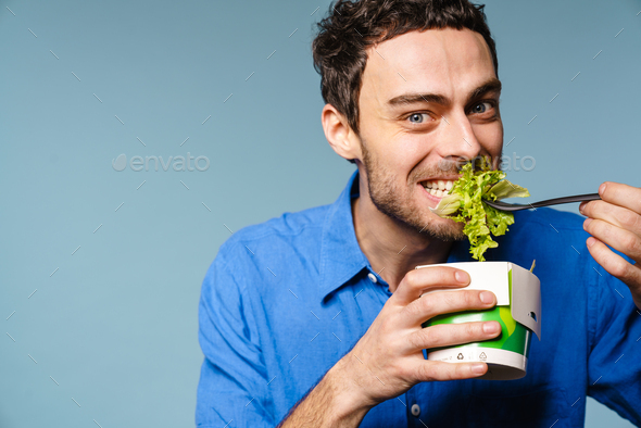 Pleased handsome guy smiling while eating salad takeaway