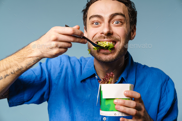 Excited handsome hungry guy eating salad takeaway