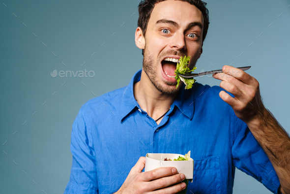 Excited handsome hungry guy eating salad takeaway