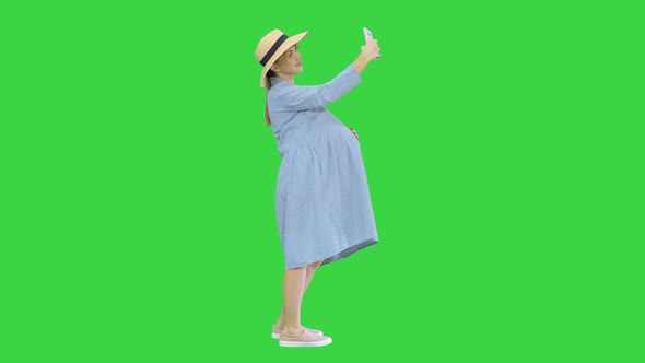 Happy Pregnant Woman in a Hat Using Her Smartphone Doing Selfie on a Green Screen, Chroma Key alt