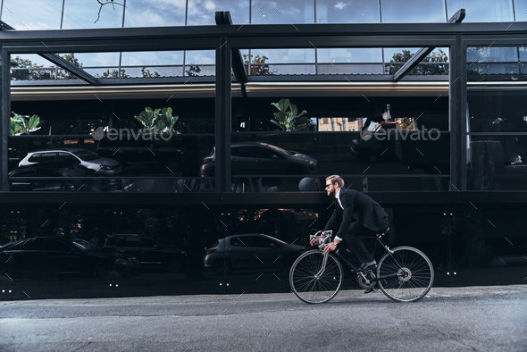 Convenient way to travel. Handsome young man in full suit hurrying to work while cycling outdoors