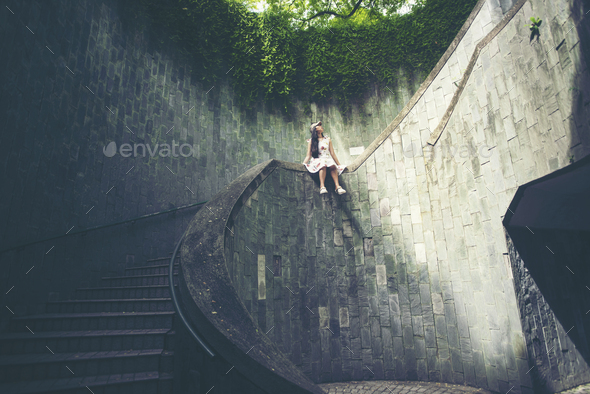 Young girl traveler sitting on circle stairs of a spiral staircase of an underground crossing