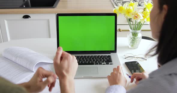 Husband and wife in kitchen video chatting with their friends or family using laptop green screen  alt