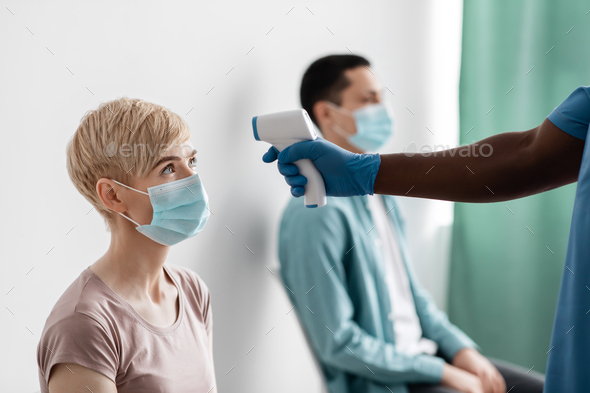 African american male nurse in protective gloves measures temperature with thermometer in adult