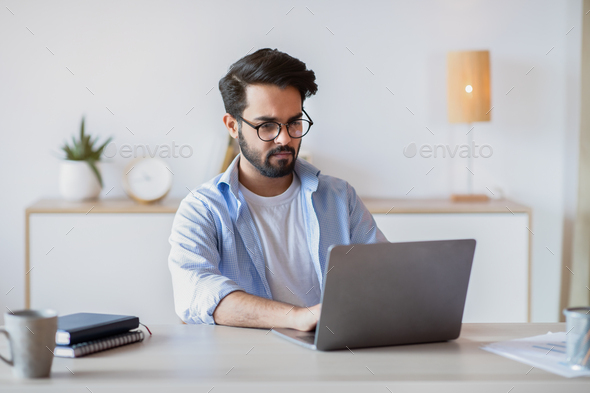 Telecommuting. Eastern Man Using Laptop Computer, Sitting At Desk In Home Office