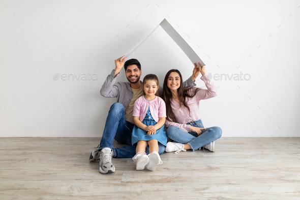 Family protection. Happy arabic family under cardboard roof sitting together on floor against white