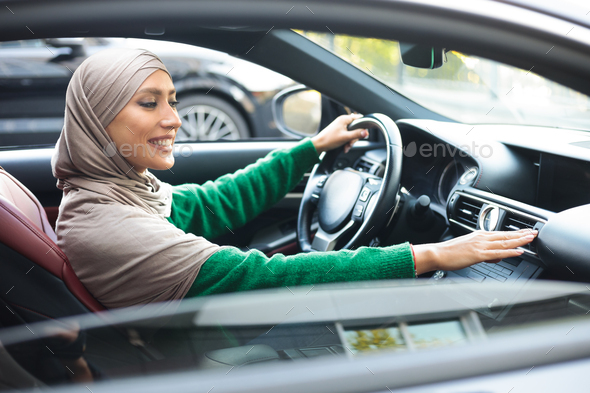 Cheerful muslim woman driving car, checking air conditioning