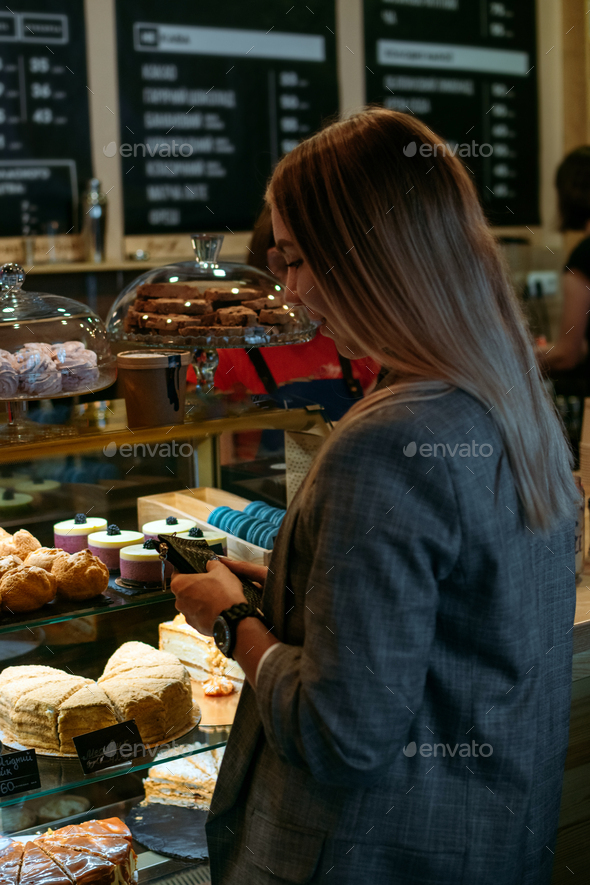 Confectionery customer, client in sweet-shop, pastry-shop. Back view of young woman choosing cake