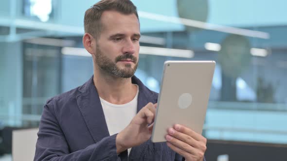 Middle Aged Businessman Browsing Internet on Tablet in Office alt