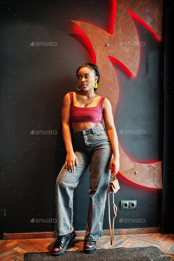 African woman in red marsala top and jeans posed indoor against wall ...