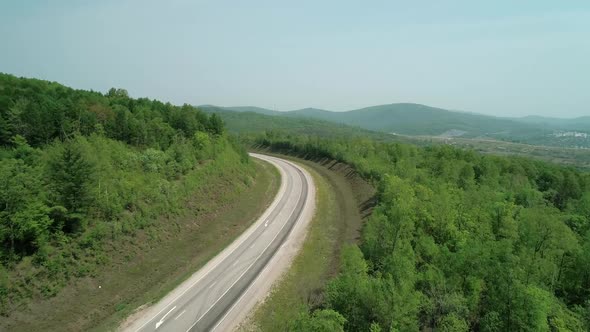 Aerial View of an Asphalt Intercity Country Road Between Green Forest with Vehicles Driving on It alt