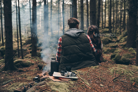 Real soul mates. Rear view of young couple warming up by the campfire while sitting in the forest