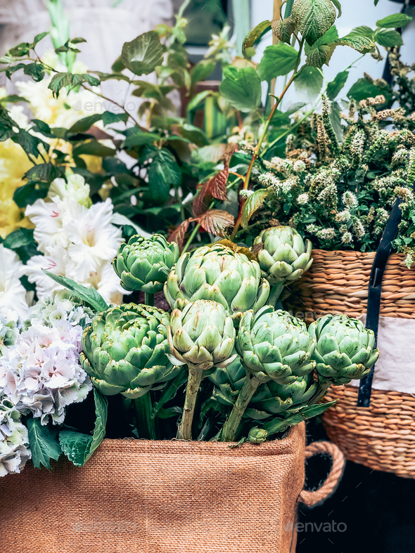 Green artichokes and flowers in small florist shop
