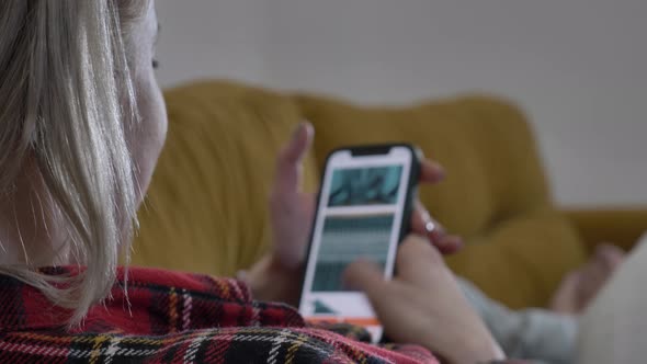 woman lying on the sofa using her phone, surfing the internet alt