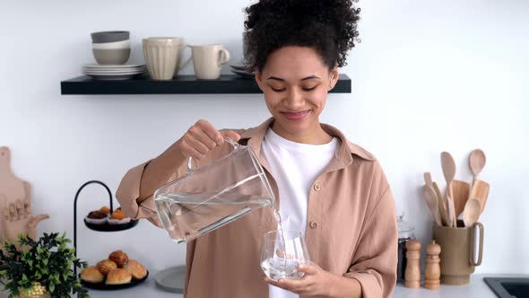 Happy Healthy African American Girl in Casual Clothes Standing at Home in the Kitchen Pouring Clean alt