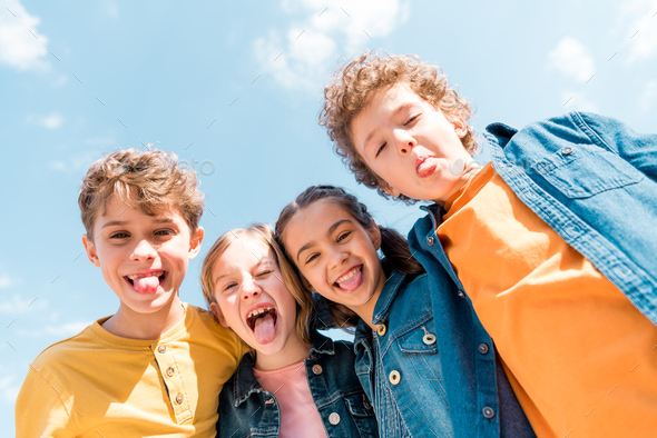 low angle view of four kids showing tongues under sky