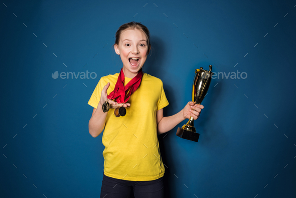excited girl with medals and trophy cup isolated on blue