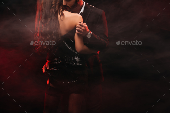 cropped view of passionate couple hugging in red smoky room