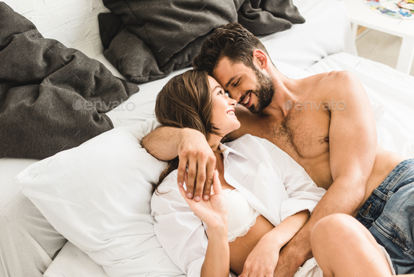 sexy young couple lying in bed, smiling and hugging while holding hands  Stock Photo by LightFieldStudios