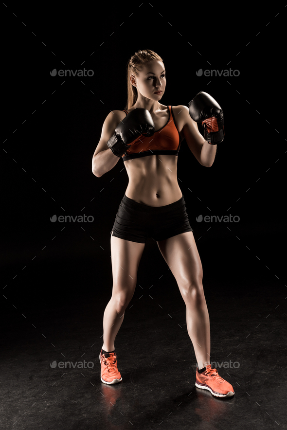 Muscular young sportswoman in boxing gloves training and looking away