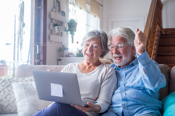 Overjoyed middle aged mature family couple looking at laptop screen, celebrating online lottery win