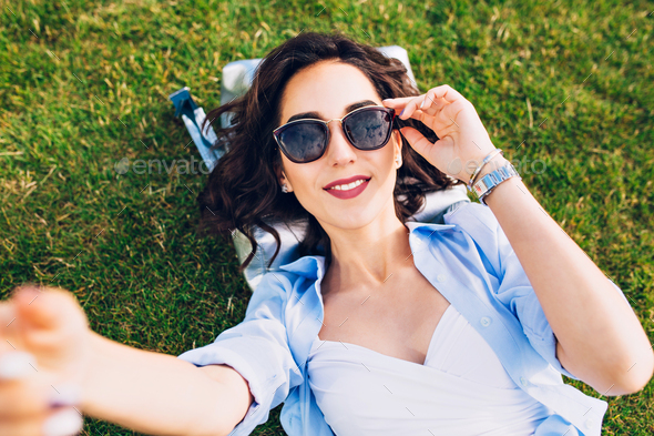 Closeup Selfie Portrait Of Cute Brunette Girl With Short Hair Laying On Grass In Park She Wears