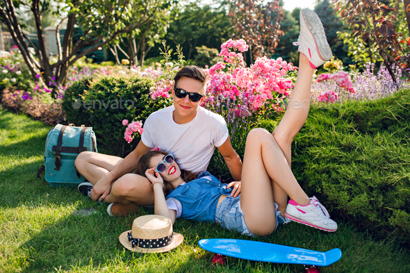 Cute couple of young people in sunglasses is chilling on grass in