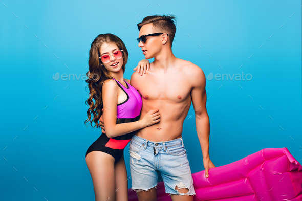 Young couple of hot guy with a bare torso hugging pretty girl with long curly hair in swimsuit on bl