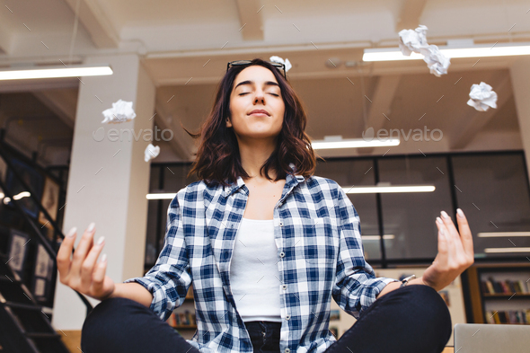 Relaxing time joyful young brunette woman having meditation on table in office surround flying paper