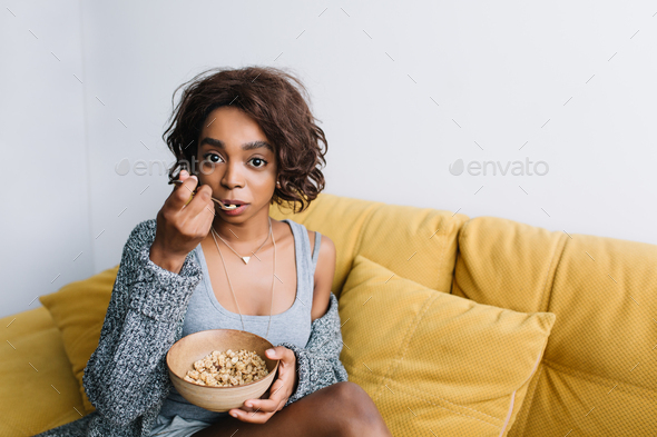 Young beautiful girl with short curly hair having healthy breakfast, eating granola, muesli on yello