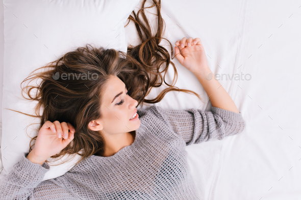 Up portrait cheerful girl with long brunette hair relaxing on white bad. Good morning, positive emot