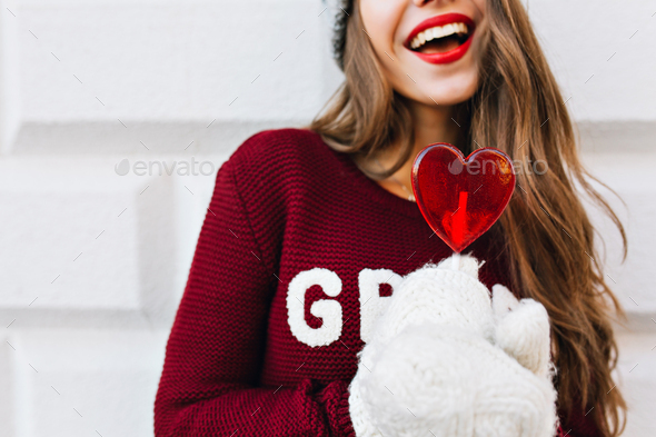 Heart red candy holding by girl in white gloves. She has long hair, snow white smile, red lips