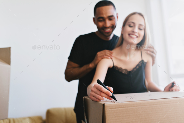 Young family moving to new house, buy apartment, flat. Cheerful couple packing boxes with books, wri