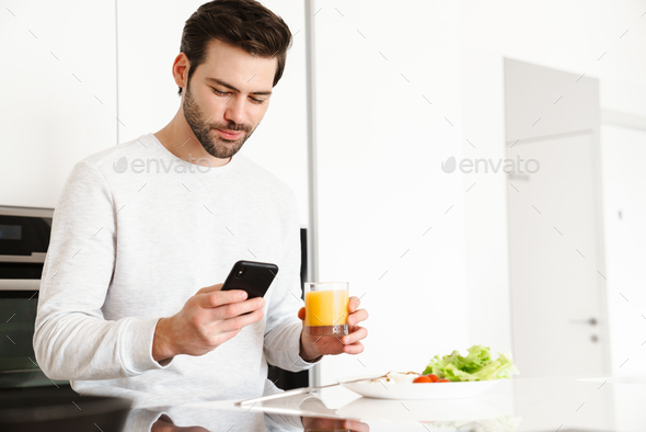 Focused handsome man using cellphone while having breakfast